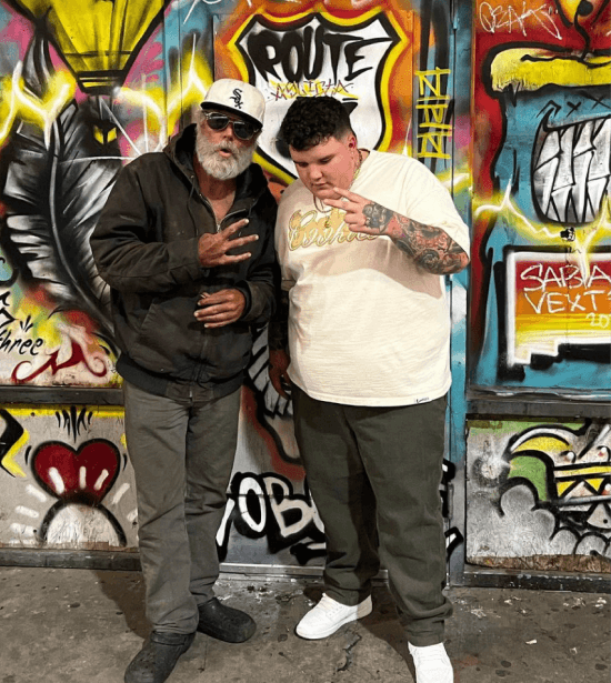 AJ Deleon posing with a man on the street in front of a mural